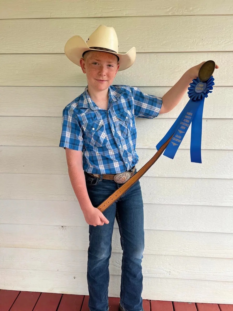 A young exhibitor in a cowboy hat holding up a blue Food Science grand champion ribbon