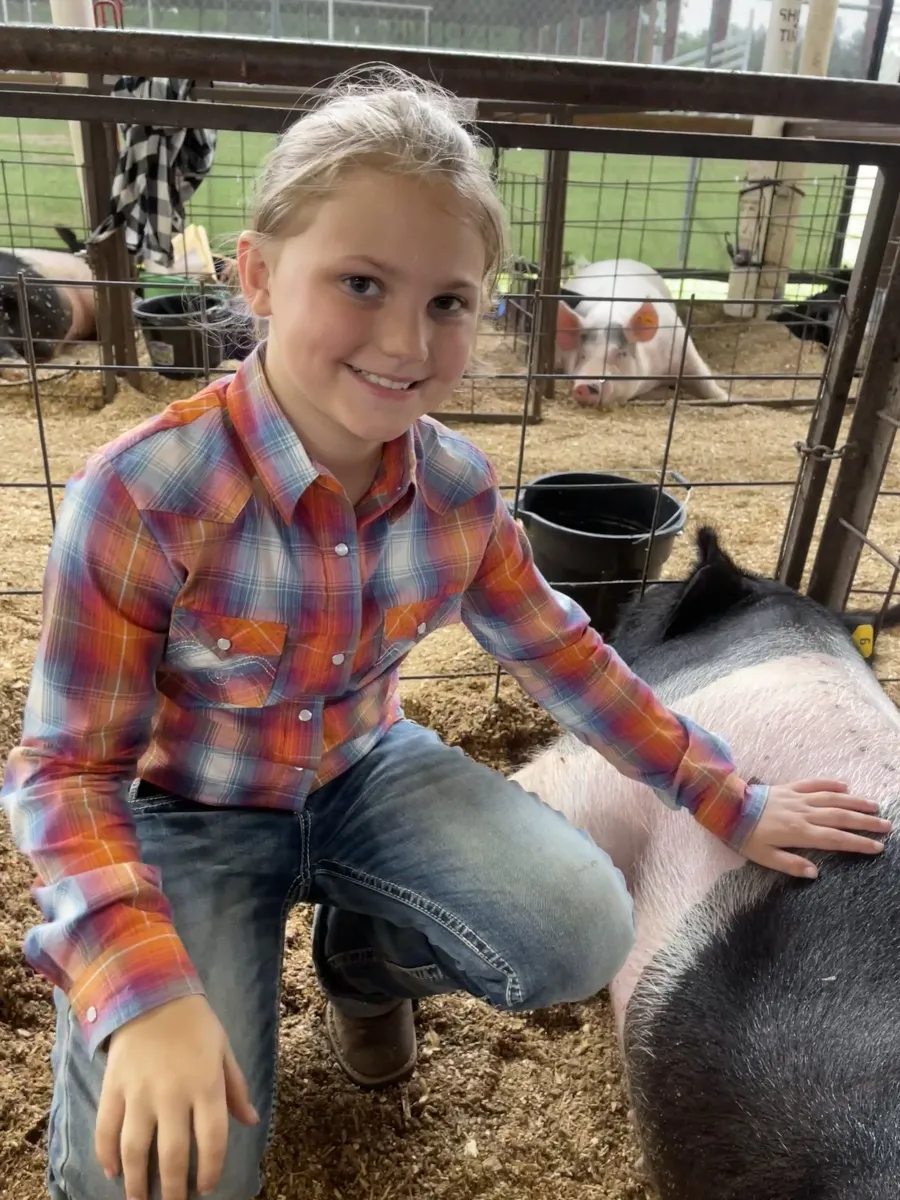 A smiling young exhibitor kneeling beside her pig in the show barn pens